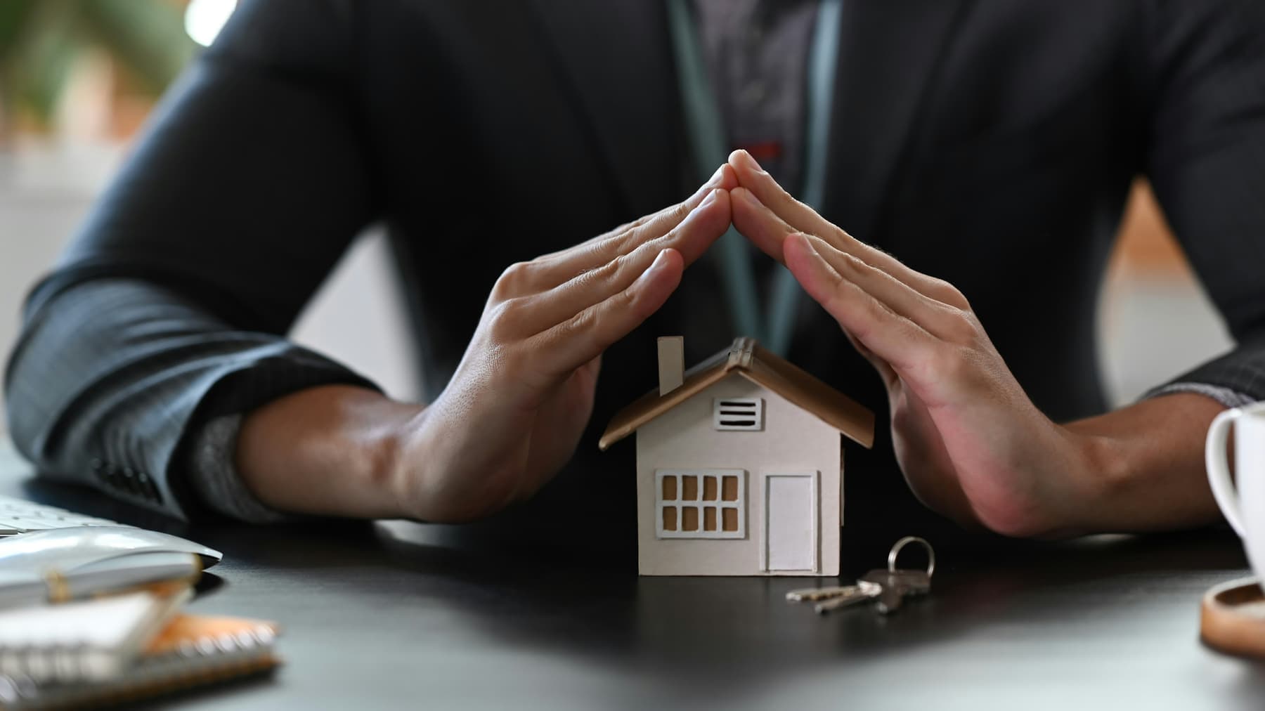 Hands protecting a model house, representing a rate switch keeping your home secure